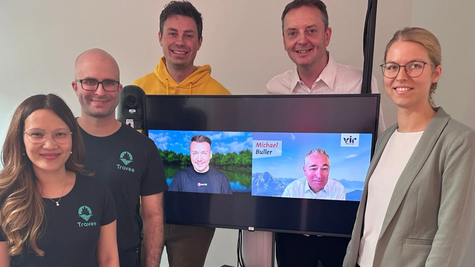 Gruppenfoto im fvw|TravelTalk-Studio: die Teams von Travee und Banaki vor einem Monitor, auf dem Viktor Waal von spotAR und VIR-Vorstand Michael Buller zugeschaltet sind