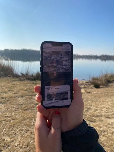 Eine Besucherin hält ihr Smartphone am Olbasee und erlebt die AR-Station zur Wandlung der Lausitzer Seenlandschaft