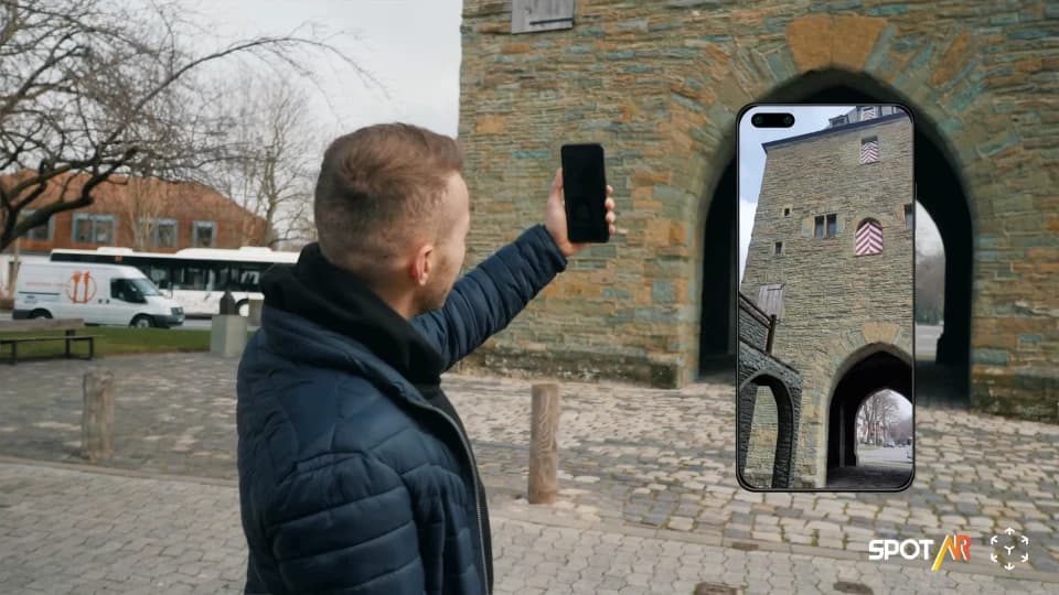 Ein Nutzer hält sein Smartphone vor das Osthofentor in Soest und sieht das Stadttor in seiner historischen Ansicht per AR